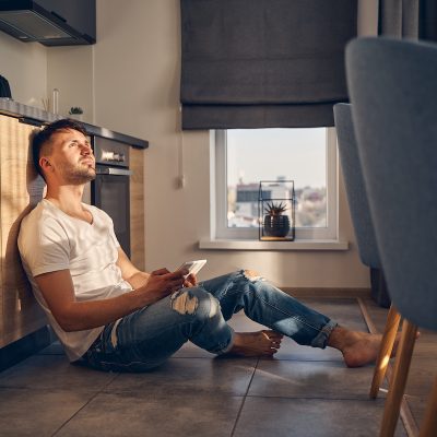 Handsome Caucasian male sitting on the floor with his mobile and contemplating about something pleasant