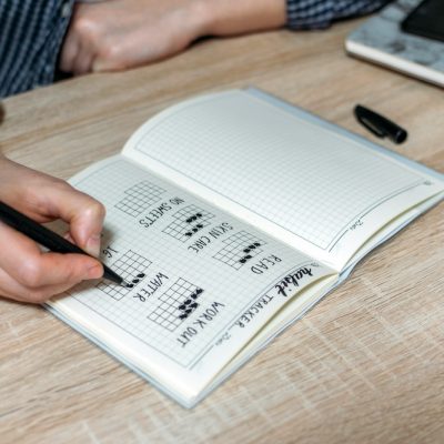 Bullet Journal, Habit Tracker. Female hand notes in habits tracker. Woman cross off day with routine in her Habit Tracker. Selective focus.