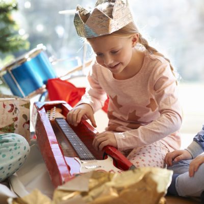 Girl and brother on living room floor gazing at toy guitar christmas gift