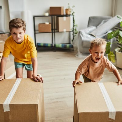 Portrait of two boys moving cardboard boxes while family relocating to new house, copy space
