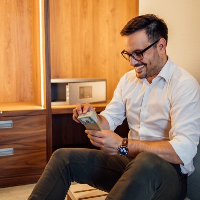 Portrait of a handsome happy businessman holding stack of money. Counting banknotes before putting it into safe deposit box.