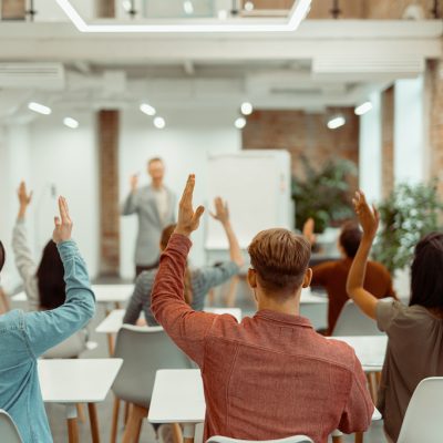 Back view of students raising their hands during lecture in the classroom